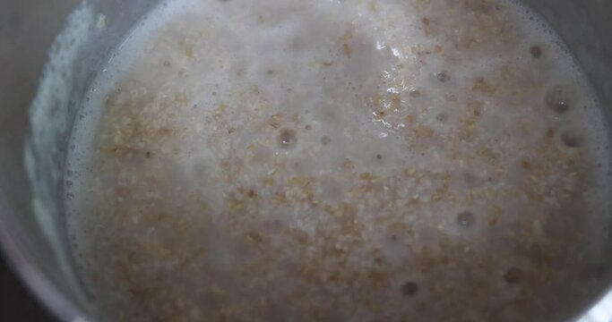 Boiling steel cut oats in pan. Bubbles pop in the oatmeal being cooked for breakfast