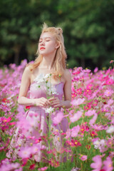 Fototapeta na wymiar Beautiful girl in a field of cosmos flowers on a sunny day