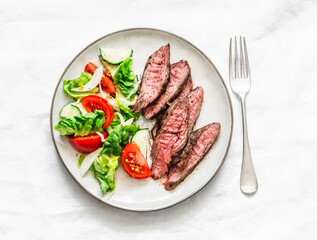 Delicious lunch - lettuce, cucumber, tomato salad and beef steak on a light background, top view