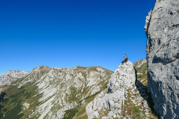 A man with a hiking backpack sitting on the of a big boulder on the way to Hohe Weichsel in Austria, with a panoramic view on a vast valley.  Narrow pathway. He is enjoying the view. Discovering