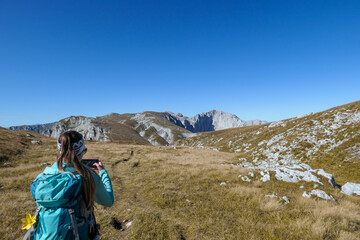 Woman with a hiking backpack taking pictures with her smartphone while hiking along a narrow pathway to the top of Hohe Weichsel in Austria. The woman in enjoying the calmness and peace. Lush pasture