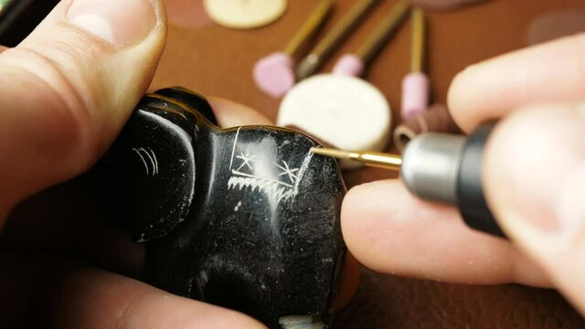 A professional engraver creates a piece of jewelry by making grooves with a special cutter.
