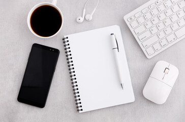 Workplace table with notebook, coffee cup, keyboard, mouse and mobile phone on marble background.
