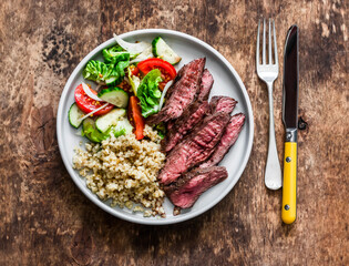 Delicious lunch - bulgur, fresh vegetable salad and steak on a wooden background, top view