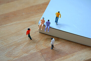 Miniature figurine character: two people sitting, one person standing on a book and two people standing on wooden floor for meeting or discussion