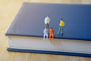 Miniature figurine character: Two people sitting and 2 people standing on blue book for meeting or discussion