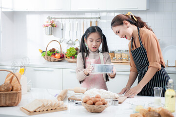 Happy Asian adorable daughter is learning and helping her mother to Sift the flour and knead the dough to make a bakery in the kitchen.It is a hobby and enhances professional or small business skills