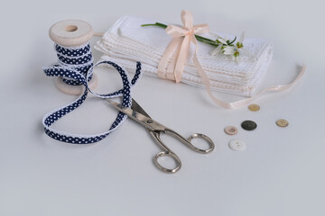 white linen napkin, trimmed with handmade lace, rolled in several layers, delicate snowdrop flower, scissors, buttons, ribbon is on light table, concept of needlework