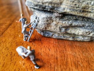 Miniature figurine character as engineering working on rock mountain with ladders, cart. They are set on wooden floor