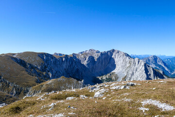 A panoramic view on Hochschwab mountain chains from the pathway leading to Hohe Weichsel. There is a vast pasture on top of a mountain, slowly turning golden. Clear view. Blue sky above. Autumn vibe