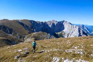 Fototapeta na wymiar A woman with a hiking backpack hiking to the top of Hohe Weichsel in Austria. The woman in enjoying the calmness. The vast pasture is turning golden. Exploration and discovery. Endless mountain chains