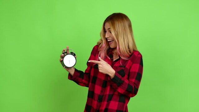 Young blonde woman holding vintage alarm clock over isolated background on green screen chroma key