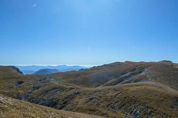 A panoramic view on Hochschwab mountain chains from the pathway leading to Hohe Weichsel. There is a vast pasture on top of a mountain, slowly turning golden. Clear view. Blue sky above. Autumn vibe