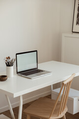 Laptop with blank copy space screen on table with stationery on table against white wall. Minimalist home office workspace. Mockup template.