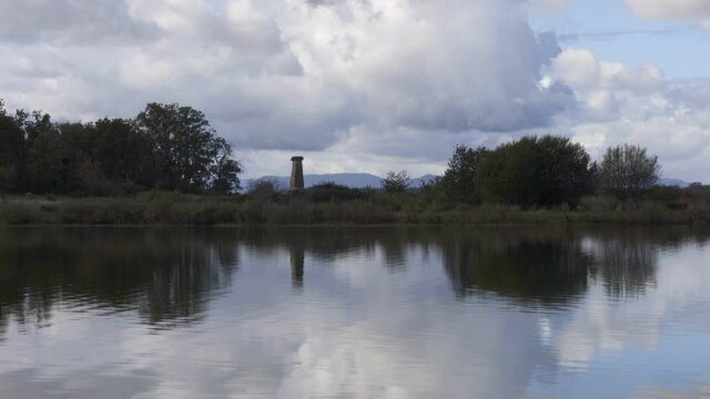 Lake dam landscape with reflection of Gardunha mountains, trees and an obelisk on a cloudy day in Santa Agueda Marateca Dam in Portugal