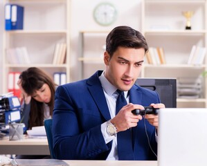 Man playing games in office while colleague is busy