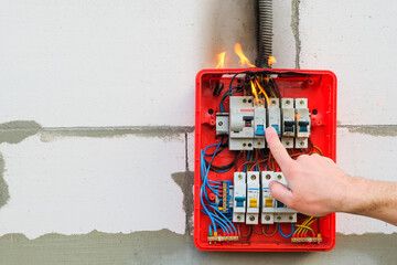 Male hand turns off burning switchboard from overload or short circuit on wall. Circuit breakers on fire from overheating due to poor connection or poor quality wires. Copy space