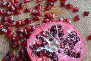 A half pomegranate and its juicy seeds on a wooden background. Pomegranate cross-section top view