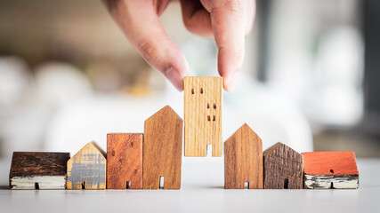 Hand choosing mini wood house model from model on wood table, selective focus, Planning to buy...