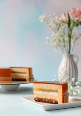 A piece of mousse cake on a plate with cake and flowers in a vase