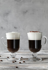 Two glasses of Irish coffee with cream foam with coffee beans and chocolate