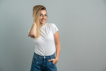 Attractive young girl wearing glasses posing beautifully on a background of gray wall. Young woman on a blank wall playfully smiling