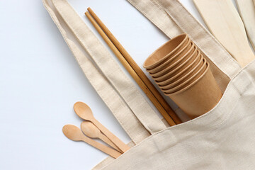 Wooden kitchen utensils in eco bag on white table background. Flat lay composition with plastic free set, cotton bag, and recycled tableware. Zero waste, eco friendly concept. Top view, copy space

