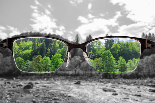 Colorful view of river and forest focused in women's glasses and monochrome background. View through eyeglasses. Better vision concept. Different world perception.