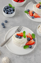 Mini Pavlova meringue cake with whipped cream and fresh berries on top on a plate on a gray concrete background. Summer dessert. Copy space.