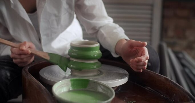 Potter paints a jug with a big brush on a potter's wheel, video from pottery workshop, ceramist makes ceramics in slow motion, 4k 60p Prores HQ 10 bit