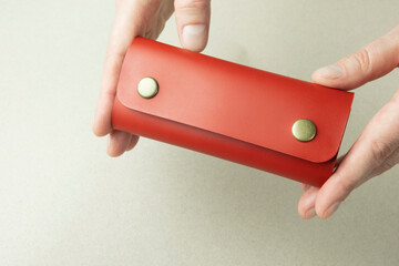 bright red leather wallet in open female hands close-up on a gray background with shadows