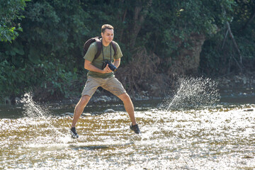 A young man dancing on the water on a sunny day, on a mountain river. © NAIL BATTALOV