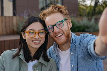 Young smiling friends wearing stylish eyeglasses taking selfie on the street. Portrait of beautiful...