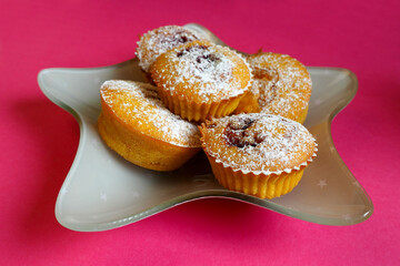 five muffins sprinkled with powdered sugar lie on a gray plate in the shape of a star on a pink background side view . homemade cakes