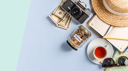 Top view of travel accessories when planning a trip: a camera, a notebook, a cup of tea. Space for text and a jar of coins