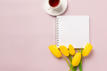 An empty notepad for writing and yellow tulips on a pink background. Spring composition with flowers