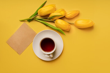 Fototapeta na wymiar Still life with yellow tulips and a mug of tea with an envelope on a yellow background