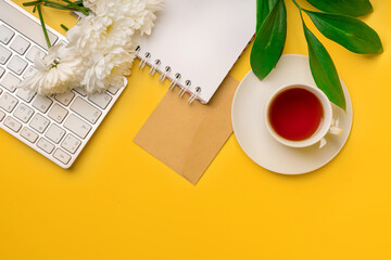 Flat lay top view office desk. Workspace with keyboard, office supplies and cup of tea. Background with green leafs on yellow background.