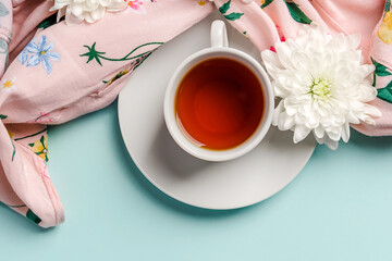 White chrysanthemums flowers on a woman's shirt and a mug of tea on a light blue background