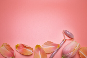 Beauty background. Rose quartz face roller and petals on the pink background, with free space for text. Facial massage tool. Top view, elegant flat lay. 