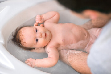 Fototapeta na wymiar A little cute baby bathes in warm water in a bath in the hands of a caring father. The concept of child care and child care