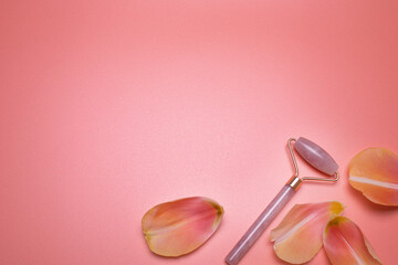 Beauty background. Rose quartz face roller and petals on the pink background, with free space for text. Facial massage tool. Top view, elegant flat lay. 