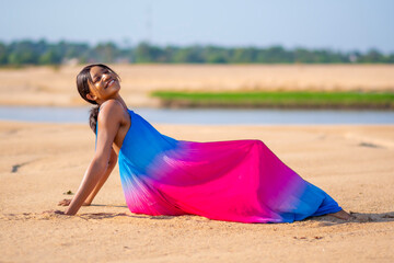 young african woman sitting on the beach sand, wearing a colorful dress, smiling and having fun, enjoying her vacation