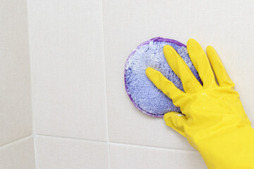 A woman's hand in a yellow glove cleans the tiles in the bathroom with detergent.Cleaning the house.Cleaning of dirty plaque