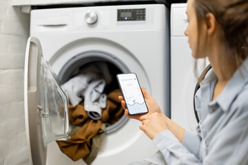 Woman controls washing machine with a smartphone