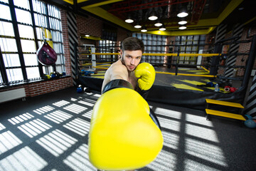 The assembled athlete in the boxing gym practices boxing punches during training and looks at the camera