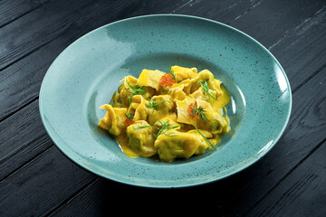 Homemade and mouth-watering ravioli with salmon and caviar, served with custard sauce in a blue plate on a dark wood background. Dish of italian cuisine