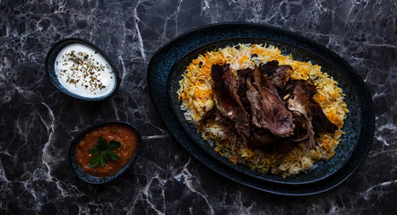 A plate of kabsa rice and grilled lamb and two small plates of Yogurt and hot sauce.