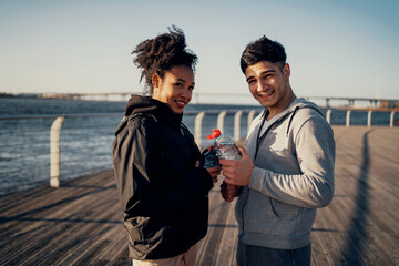 a contented Afro woman and an Italian man drink water. Time for outdoor sports in the park in the...