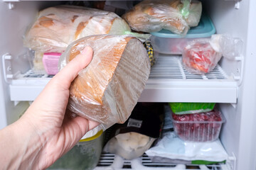 A hand putting a package of brown bread in reserve on a shelf of a home freezer, long life food storage concept